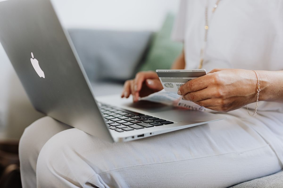 Person sitting with a laptop on their lap while holding up the back of a grey bank card
