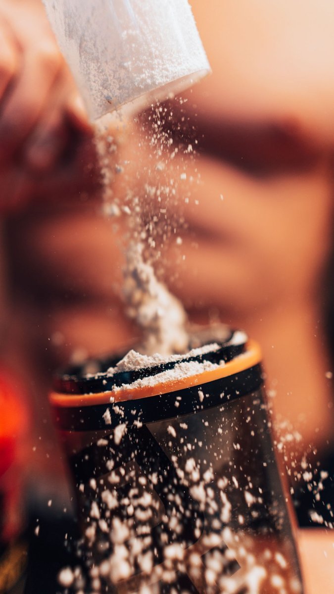 Powder being poured from a scoop into a shaker bottle