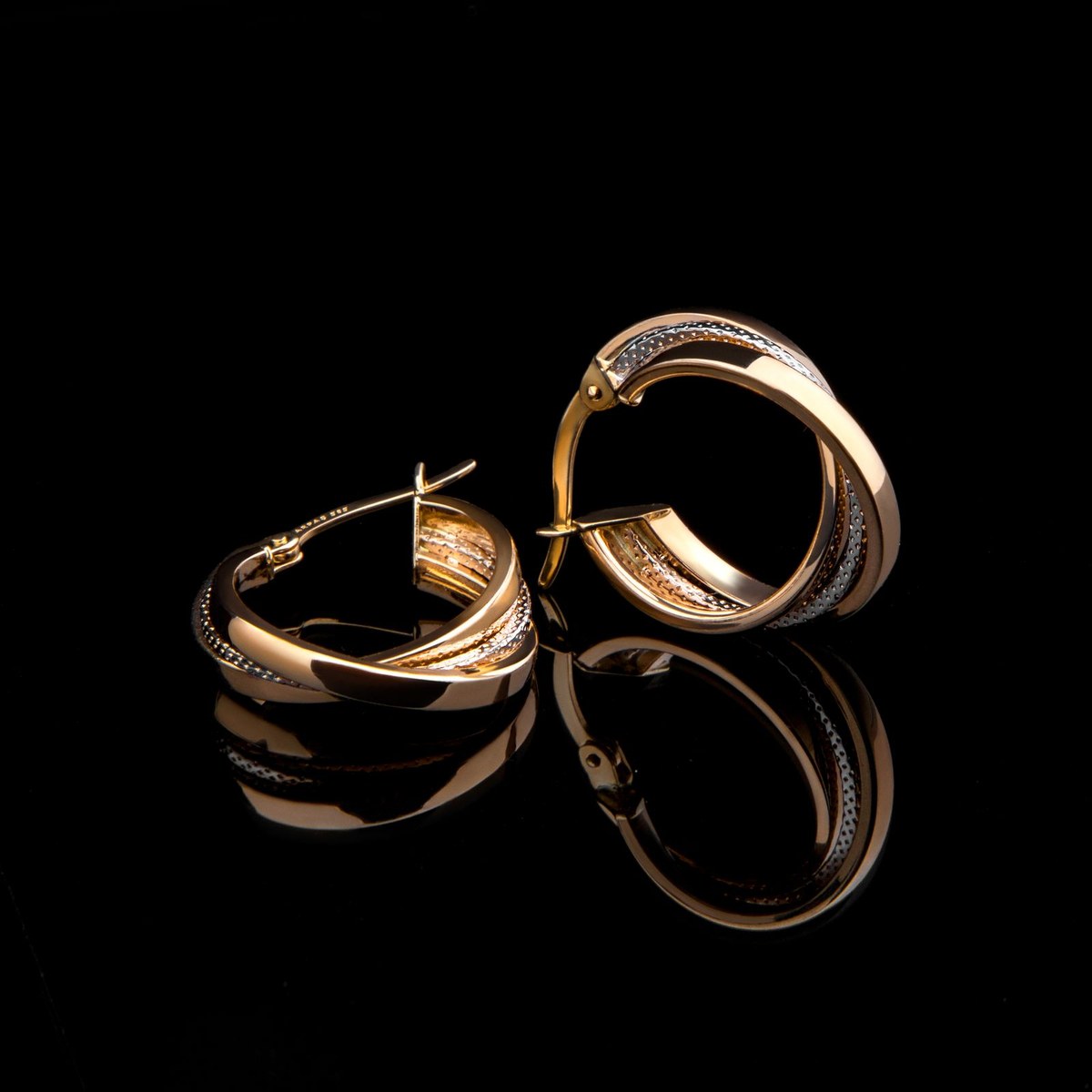 Two-tone yellow and white gold hoop earrings on a reflective black studio surface
